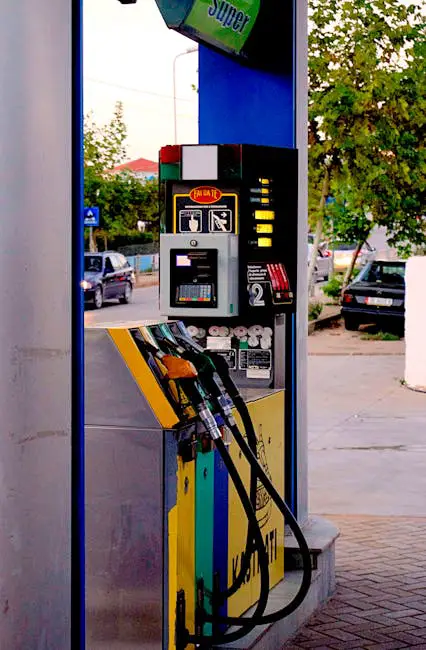 Fuel pumps at a modern gas station on an urban street, with vehicles and trees visible.