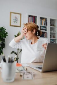 Worried woman counting expenses on a laptop while holding a receipt at her desk.