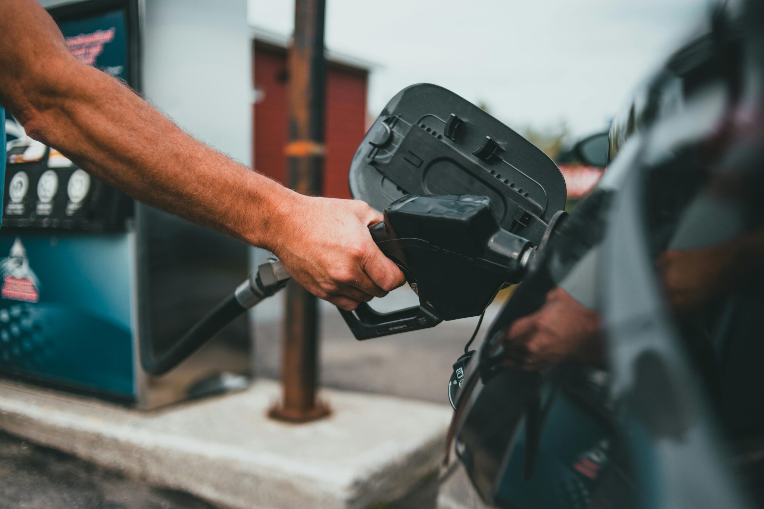 Close-up of a hand holding a nozzle while refueling a car at a gas station.